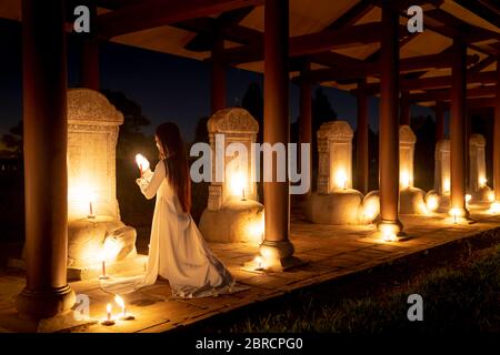 Hue City, Thua Thien Hue Province, Vietnam - 7 maggio 2020: Un'immagine di una ragazza in un tradizionale ao dai sta pregando in un tempio circondato da un sacco di bagliore Foto Stock