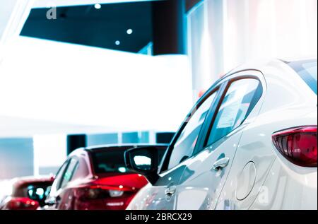 Vista posteriore di auto di lusso bianca parcheggiata in showroom moderno per la vendita. Auto bianca brillante su auto sfocata in showroom. Concessionaria di automobili. Impatto del coronavirus Foto Stock