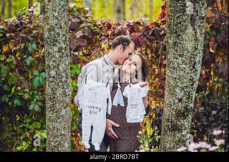 Una giovane donna incinta e suo marito. Una famiglia felice appeso vestiti per il bambino ad asciugare su una corda. Donna incinta rilassarsi nel parco. Foto Stock