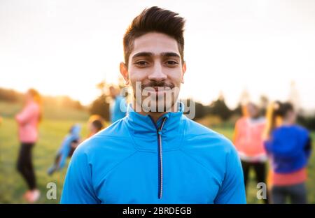 Un ritratto di giovane con un grande gruppo di persone che fanno esercizio in natura. Foto Stock