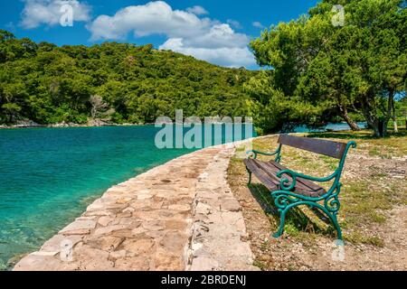 Una panca rustica in legno e ferro battuto accanto a un sentiero in pietra a piedi sull'isola di Santa Maria nel lago Veliko Jezero, nel Parco Nazionale di Mljet, Croazia. Foto Stock