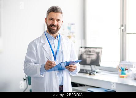 Dentista maturo nella moderna chirurgia dentale, guardando la macchina fotografica. Foto Stock