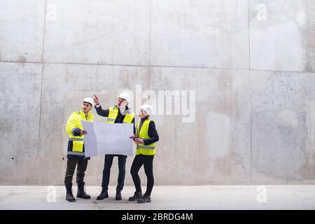 Un gruppo di ingegneri che si trova contro una parete in cemento nel cantiere. Foto Stock