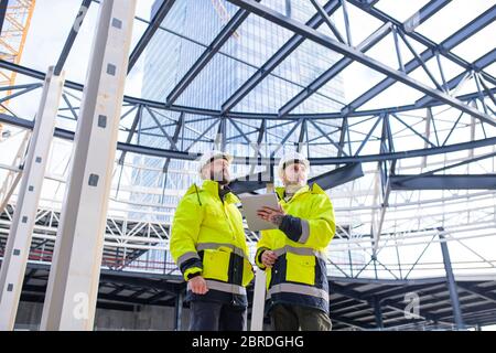 Uomini ingegneri in piedi all'aperto in cantiere, utilizzando tablet. Foto Stock