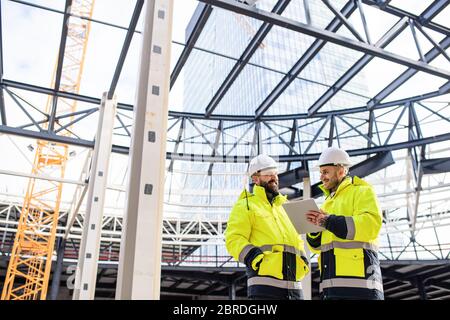 Uomini ingegneri in piedi all'aperto in cantiere, utilizzando tablet. Foto Stock