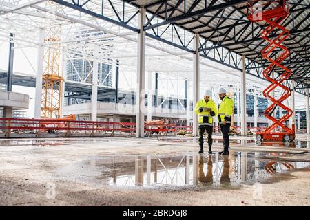 Uomini ingegneri in piedi all'aperto in cantiere, utilizzando tablet. Foto Stock