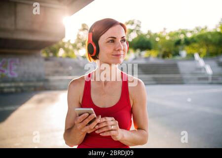 Giovane donna runner con cuffie in città, utilizzando smartphone. Foto Stock