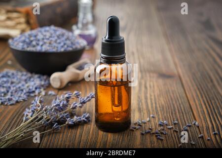 Flacone contagocce di olio essenziale di lavanda. Ciotola di fiori secchi di lavanda su sfondo. Foto Stock