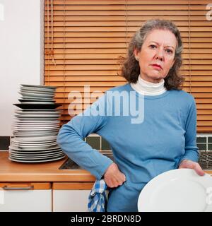 Donna mano che lava grande pila di piatti, cercando annoiato Foto Stock