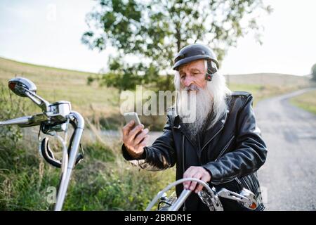 Un uomo anziano con moto in campagna, prendendo selfie. Foto Stock