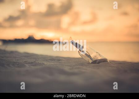 Messaggio in bottiglia lavato a terra contro il tramonto. Sfondo di design tropicale della spiaggia del tramonto. Castaway, solitudine, concetto perso Foto Stock
