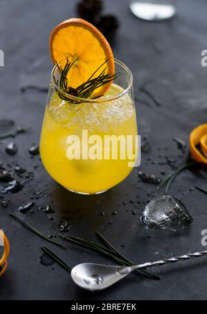 fuoco selettivo, rinfrescante limonata fatta in casa arancione con ghiaccio e fette di frutta, in una luce sagomata su un tavolo scuro Foto Stock