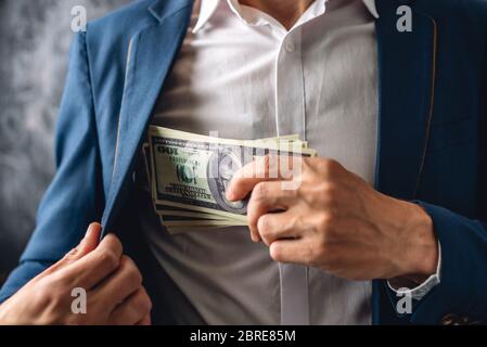 Uomo in un vestito mettendo un wad di cento-dollari fatture nella tasca interna della sua giacca. Primo piano. Il concetto di corruzione e di corruzione dei funzionari Foto Stock