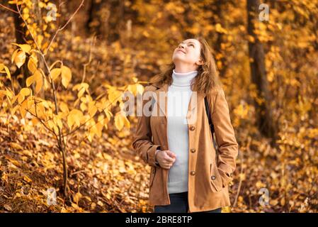 Donna in pullover bianco e giacca beige nel parco autunnale. Felice ragazza adulta che cammina nella foresta autunnale. Donna sola giovane in natura il giorno dell'autunno. Concetto o Foto Stock