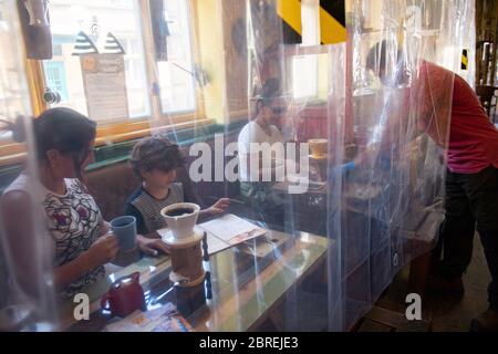 Il proprietario del caffè Francini Osorio serve i clienti in una fase di prova durante il blocco del coronavirus. Osorio ha installato un purificatore d'aria e 35 tende da doccia trasparenti, che divideranno i clienti e i tavoli, nel Francini Cafe De Colombia, Worcester, pronto per la riapertura della sua attività, in quanto le restrizioni di blocco sono attenuate. Foto Stock