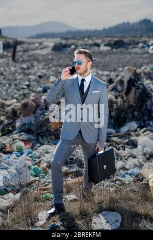 Uomo d'affari moderno in discarica, consumismo contro concetto di inquinamento. Foto Stock