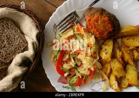 Cibo su un piatto. Semplice pranzo fatto in casa: Patate fritte, polpette e una porzione di insalata. Nutrizione sociale. Vista dall'alto Foto Stock