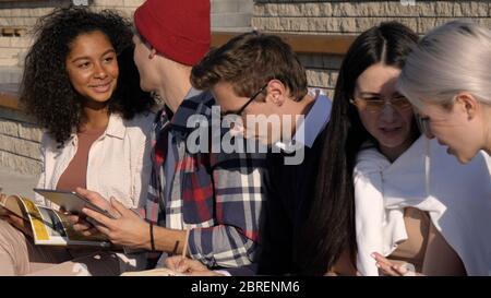 Studenti multietnici che si affacciano all'aperto facendo qualche lavoro. Foto Stock