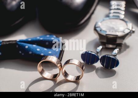 Anelli di nozze. Scarpe in pelle nera, orologio, cravatta con arco blu e gemelli, su un davanzale bianco. Foto Stock