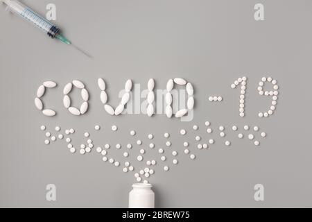 Piatto di pillole di medicina forma come parola covid 19 con siringa e pillole su sfondo grigio, concetto di assistenza sanitaria e prevenire la diffusione di pandemia Co Foto Stock
