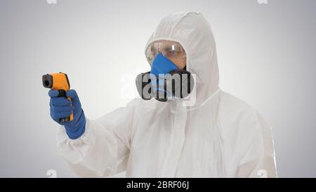 Medico usando la pistola del termometro della fronte infrarosso per controllare la temperatura corporea per i sintomi del virus covid-19 su sfondo gradiente. Foto Stock