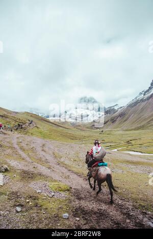 Tradizionale cavalcare il cavallo indigeno Quechua attraverso le valli della regione di Cusco del Perù, accanto alla montagna Arcobaleno (o Montaña de Siete Foto Stock