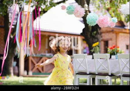 Piccola ragazza che corre all'aperto in giardino in estate, concetto di festa di compleanno. Foto Stock