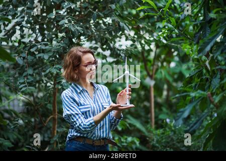 Giovane donna in piedi in giardino botanico, tenendo modello di mulino a vento. Foto Stock