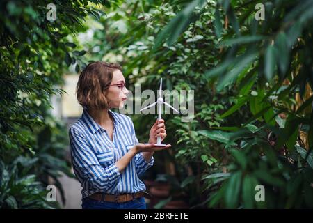 Giovane donna in piedi in giardino botanico, tenendo modello di mulino a vento. Foto Stock