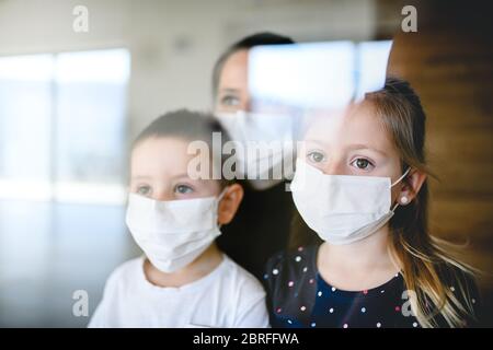 Madre e bambini con maschere al coperto a casa, virus Corona, concetto di quarantena. Foto Stock