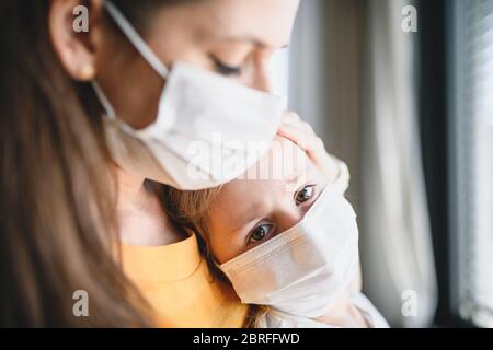 Madre e bambino con maschere al coperto a casa, virus Corona e concetto di quarantena. Foto Stock