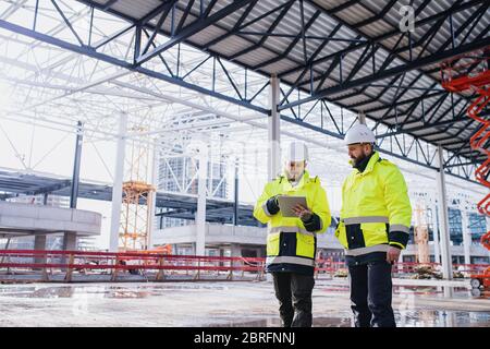 Uomini ingegneri in piedi all'aperto in cantiere, utilizzando tablet. Foto Stock