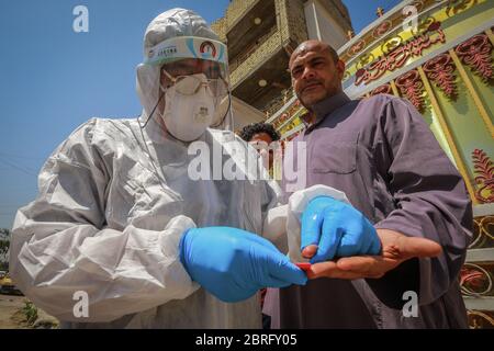 Baghdad, Iraq. 21 Maggio 2020. Un operatore sanitario del Ministero della Salute indossare tuta protettiva prende un campione di sangue da un uomo durante un esame sul campo per eseguire il coronavirus (COVID-19) test per i cittadini nel quartiere sobborgo Sadr City a Baghdad. Credit: Ameer al Mohammedaw/dpa/Alamy Live News Foto Stock