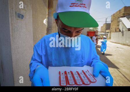 Baghdad, Iraq. 21 Maggio 2020. Un operatore sanitario del Ministero della Salute indossare tuta protettiva tiene dispositivi di analisi del sangue durante un esame sul campo per eseguire il coronavirus (COVID-19) test per i cittadini nel quartiere sobborgo Sadr City a Baghdad. Credit: Ameer al Mohammedaw/dpa/Alamy Live News Foto Stock