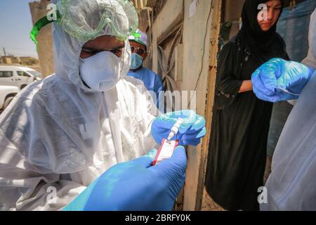 Baghdad, Iraq. 21 Maggio 2020. Un operatore sanitario del Ministero della Salute indossare tuta protettiva prende un campione di sangue da una donna durante un esame sul campo per eseguire il coronavirus (COVID-19) test per i cittadini nel quartiere sobborgo Sadr City a Baghdad. Credit: Ameer al Mohammedaw/dpa/Alamy Live News Foto Stock