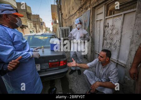 Baghdad, Iraq. 21 Maggio 2020. Gli operatori sanitari del Ministero della Salute indossare tute protettive parlare con un uomo durante un esame sul campo per eseguire il coronavirus (COVID-19) test per i cittadini nel quartiere sobborgo Sadr City a Baghdad. Credit: Ameer al Mohammedaw/dpa/Alamy Live News Foto Stock