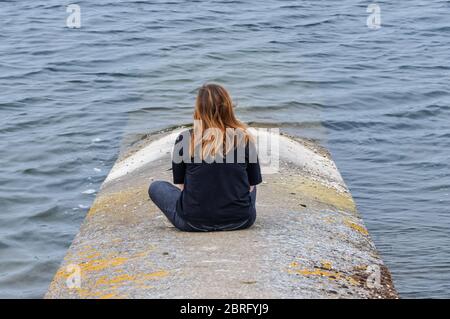 Ragazza sola seduta e guardando il lago Foto Stock