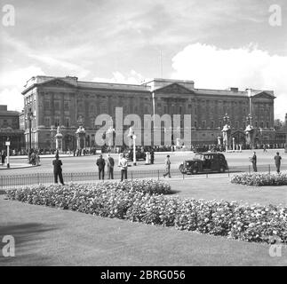 Anni '50, storici, persone che guardano fuori attraverso le porte di Buckingham Palace, Westminster, Londra, Inghilterra, Regno Unito. Inaugurato nel 1705, il palazzo è la residenza londinese e sede amministrativa della monarchia britannica, la Regina Elisabetta II Foto Stock