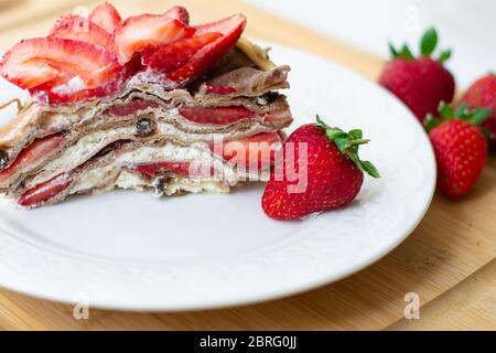 Dolce estivo leggero: Una fetta di torta crepe con panna montata, gocce di cioccolato e fragole tra gli strati. Foto Stock