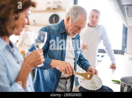 Gruppo di amici senior a cena a casa, cucina. Foto Stock