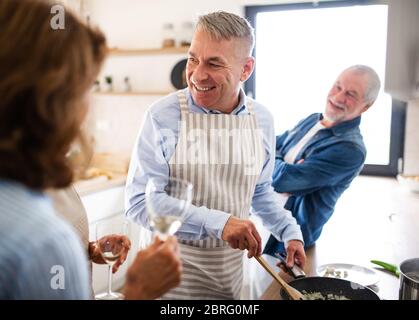 Gruppo di amici senior a cena a casa, cucina. Foto Stock
