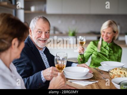 Gruppo di amici senior a cena a casa, con bicchieri di vino. Foto Stock