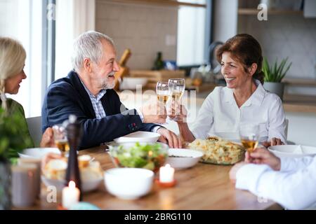 Gruppo di amici senior a cena a casa, bicchieri da clinking. Foto Stock