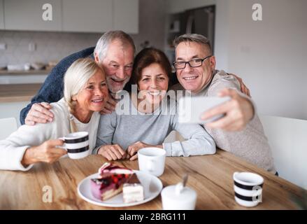 Gruppo di amici senior a casa, prendendo selfie con lo smartphone. Foto Stock