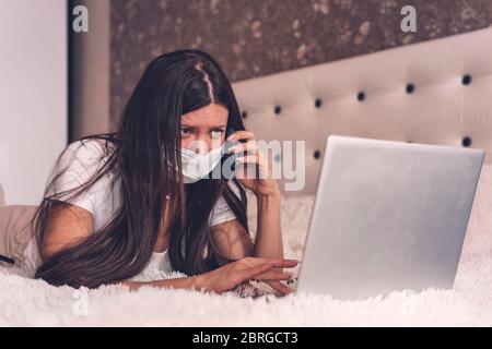 Donna malata che lavora su un computer portatile sdraiato a letto, influenza da febbre alta, riposo. Lavoro da casa, Covid-19. Lavoro a distanza. Lavoro a distanza Foto Stock