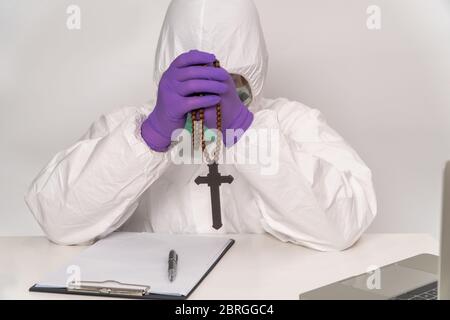 I medici in tute e maschere protettive tengono una croce e pregano per la speranza di trattare e prevenire l'infezione, il concetto di diffusione Coro Foto Stock