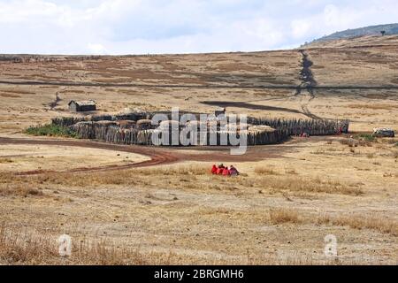 Villaggio Maasai, recinzione compatta, piccole case rotonde, tetti di paglia, gente recinzione esterna, abbigliamento tradizionale rosso, gruppi semi-nomadi tribù, collina Foto Stock