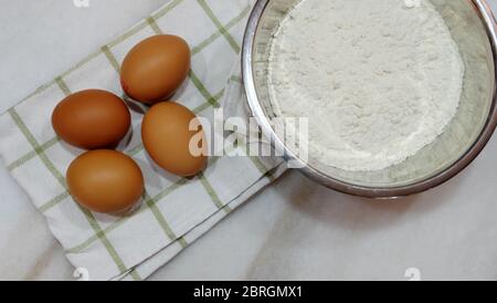 4 uova marroni su un panno da cucina bianco-verde e una ciotola di farina bianca da forno a lato. Foto Stock