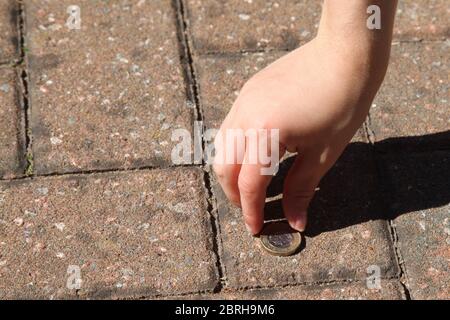 Mano del bambino che raccoglie i soldi sul pavimento, £2017 1 moneta della libbra che giace sul marciapiede Foto Stock
