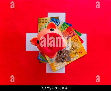 Moneta svizzera, franco svizzero.Foto di una banca piggy che guarda in cima a un'ondata di fatture svizzere su una bandiera svizzera Foto Stock